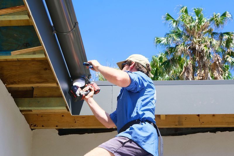 A Man is Working on a Gutter on the Side of a Building — Foreshore Plumbers in Tuncurry, NSW