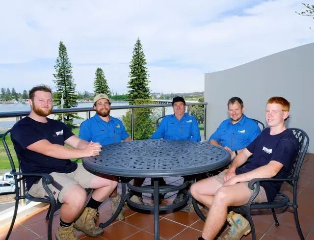 A Group of Men Are Sitting Around a Table on a Balcony — Foreshore Plumbers In Hallidays Point, NSW