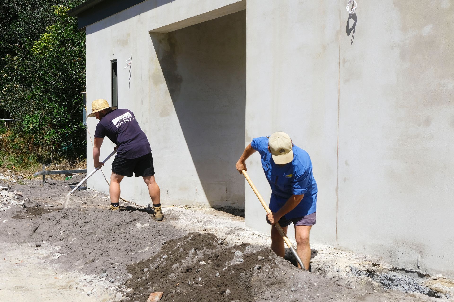 Two Men Are Digging in the Dirt in Front of a Building — Foreshore Plumbers In Hallidays Point, NSW