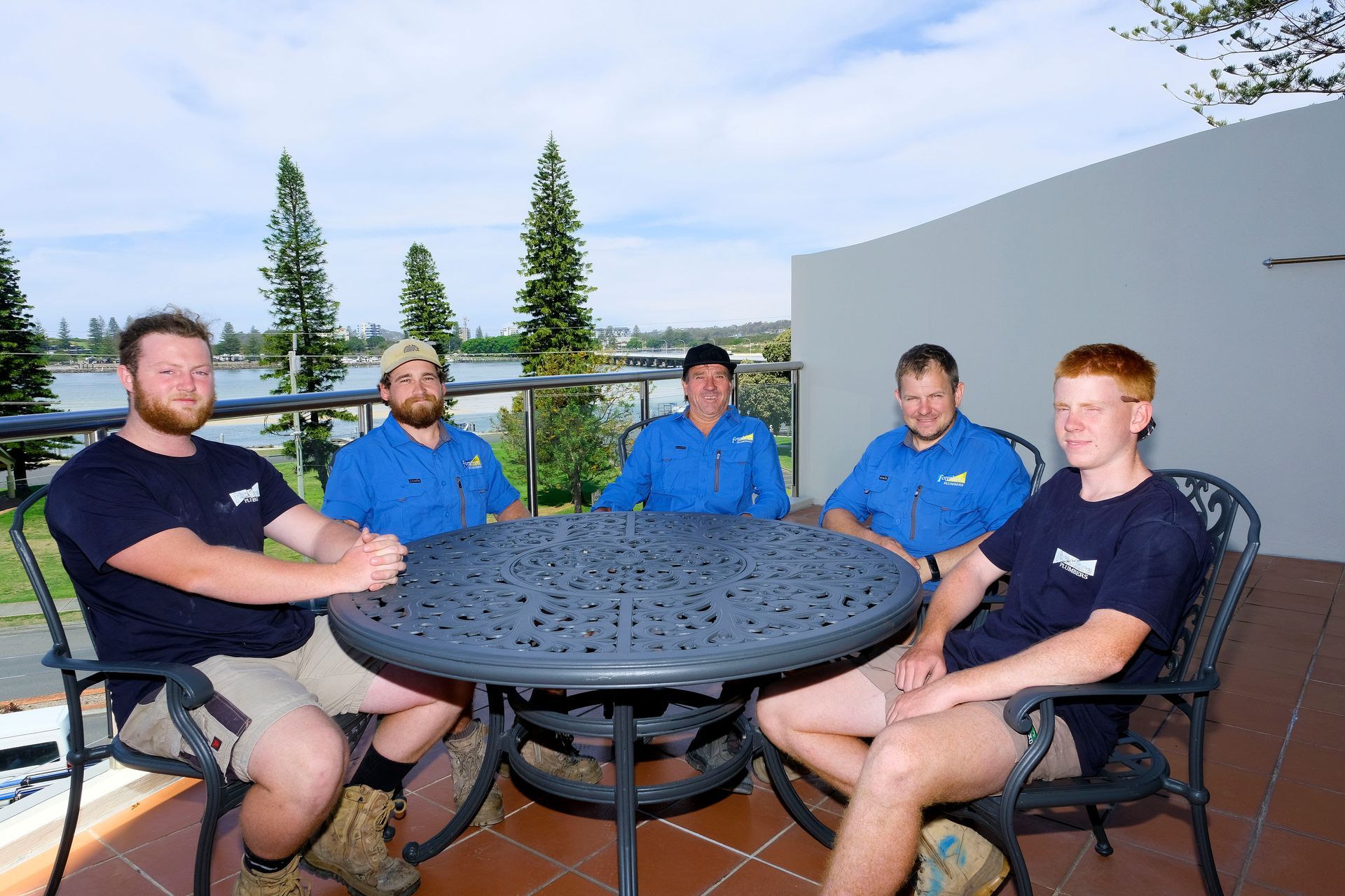 A Group of Men Are Sitting Around a Table on a Balcony — Foreshore Plumbers In Tuncurry, NSW