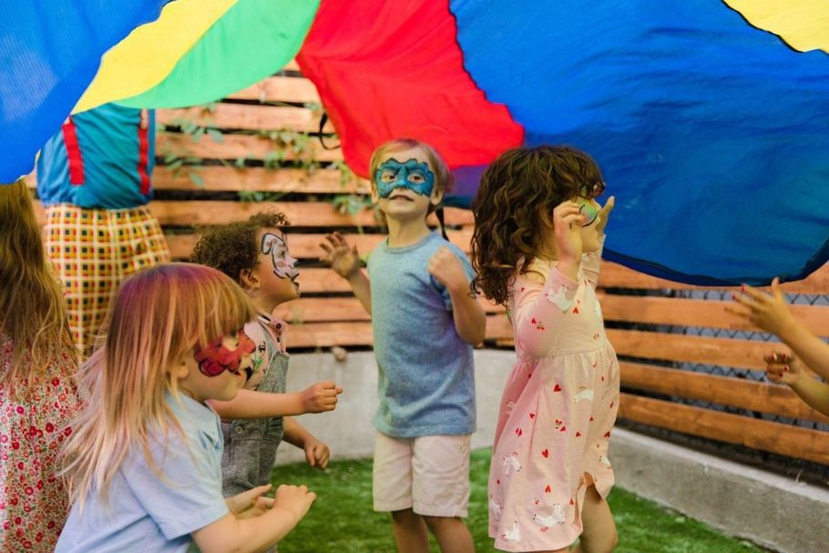Children playing under a colorful parachute outdoors, reaching up in a grassy yard