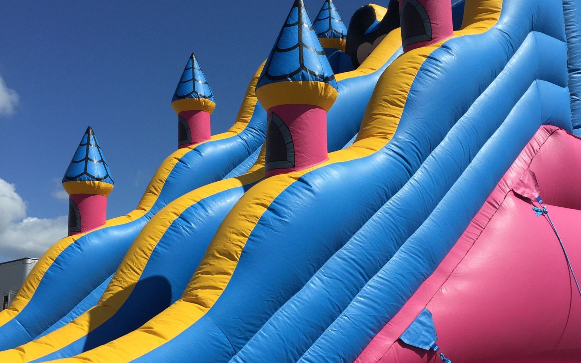 Blue and pink inflatable slide with castle turrets against a cloudy sky