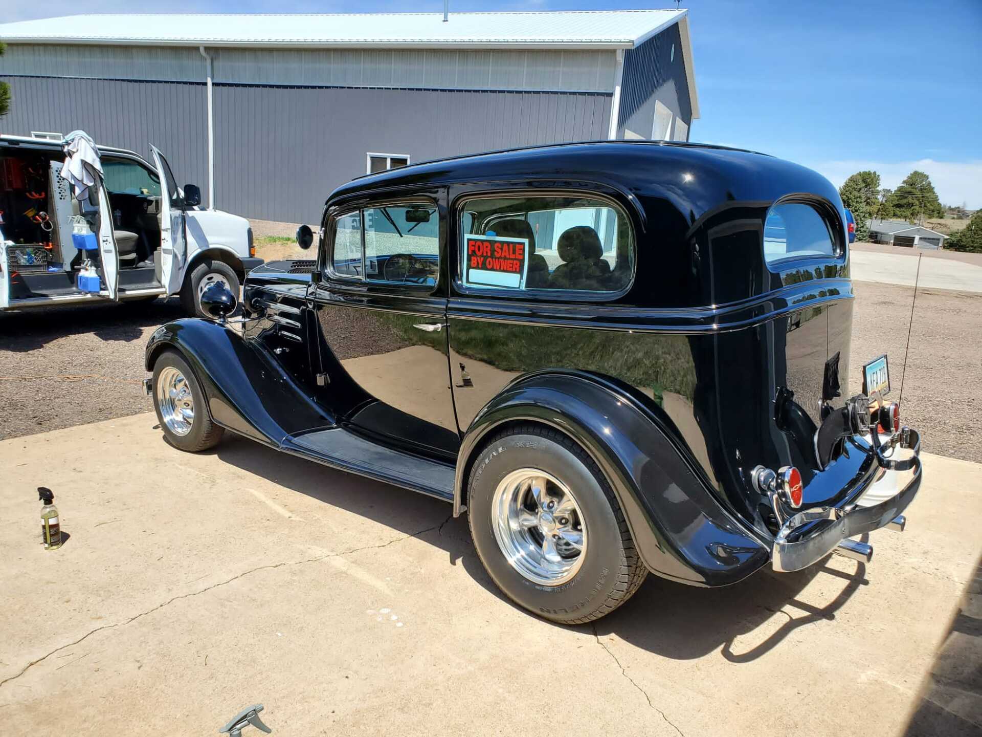 a black vintage car parked in a parking lot next to a truck .