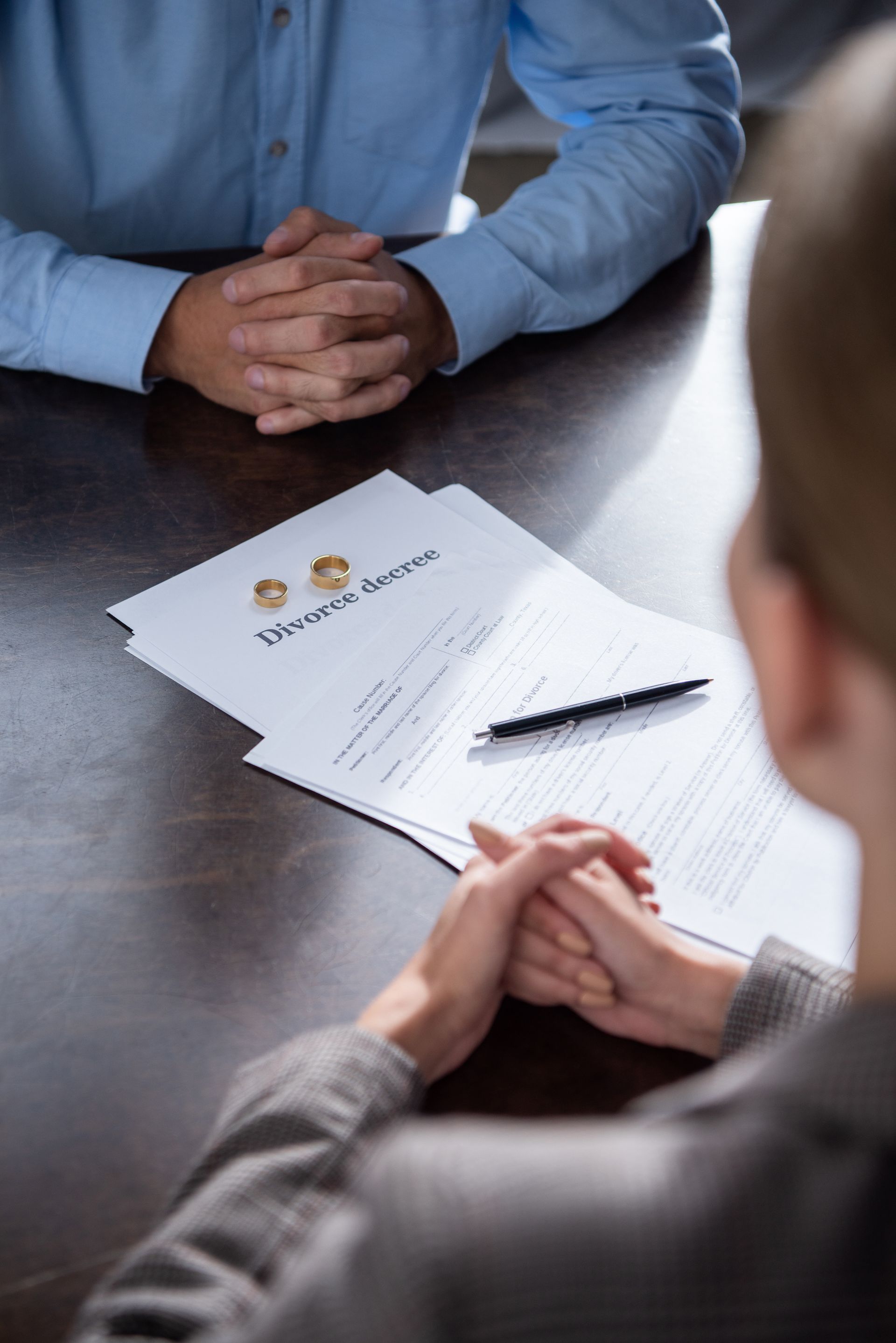 Divorce papers with rings, a pen, and two people at a table, hands clasped.