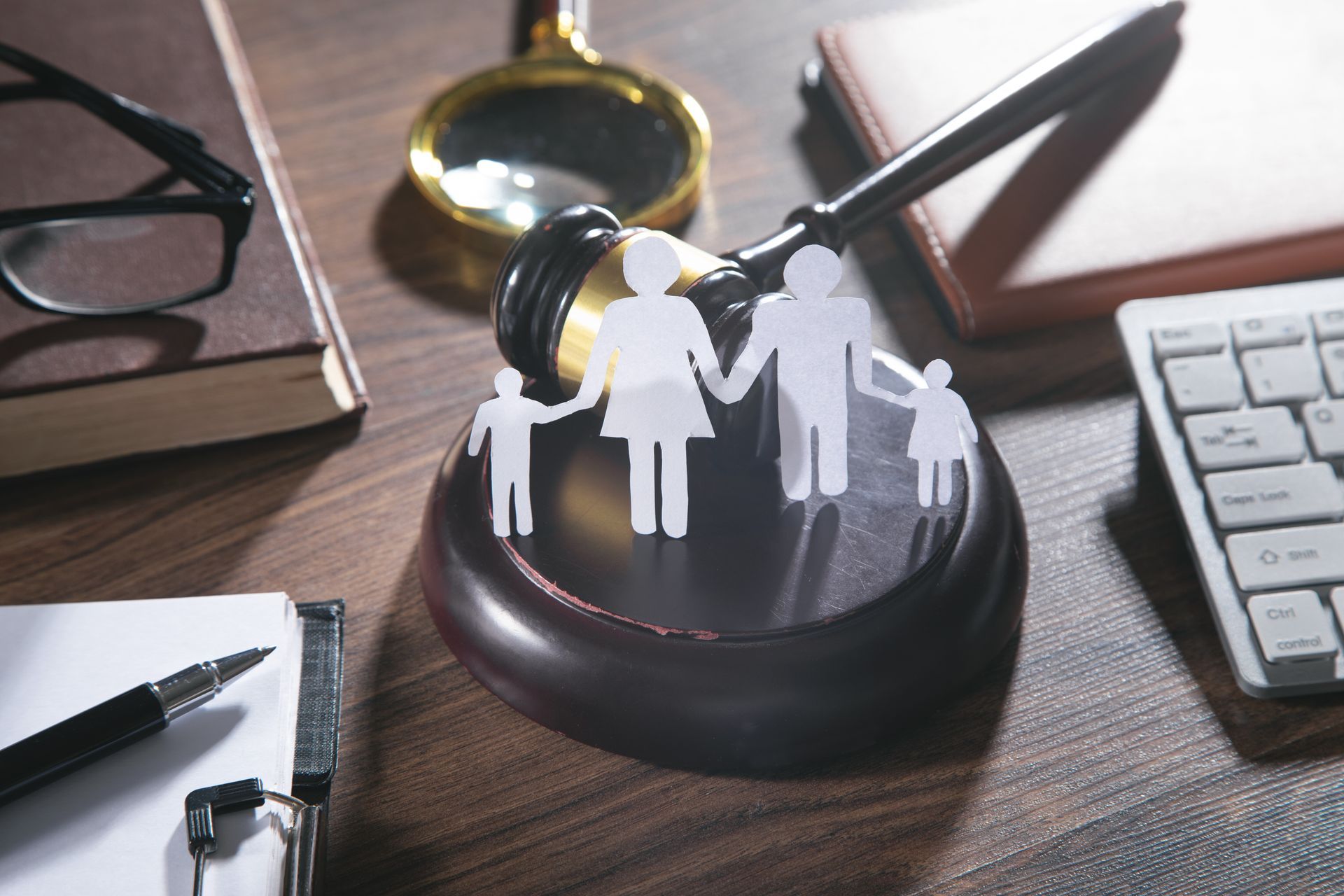 Paper family figures standing on a judge's gavel with legal items on a desk.