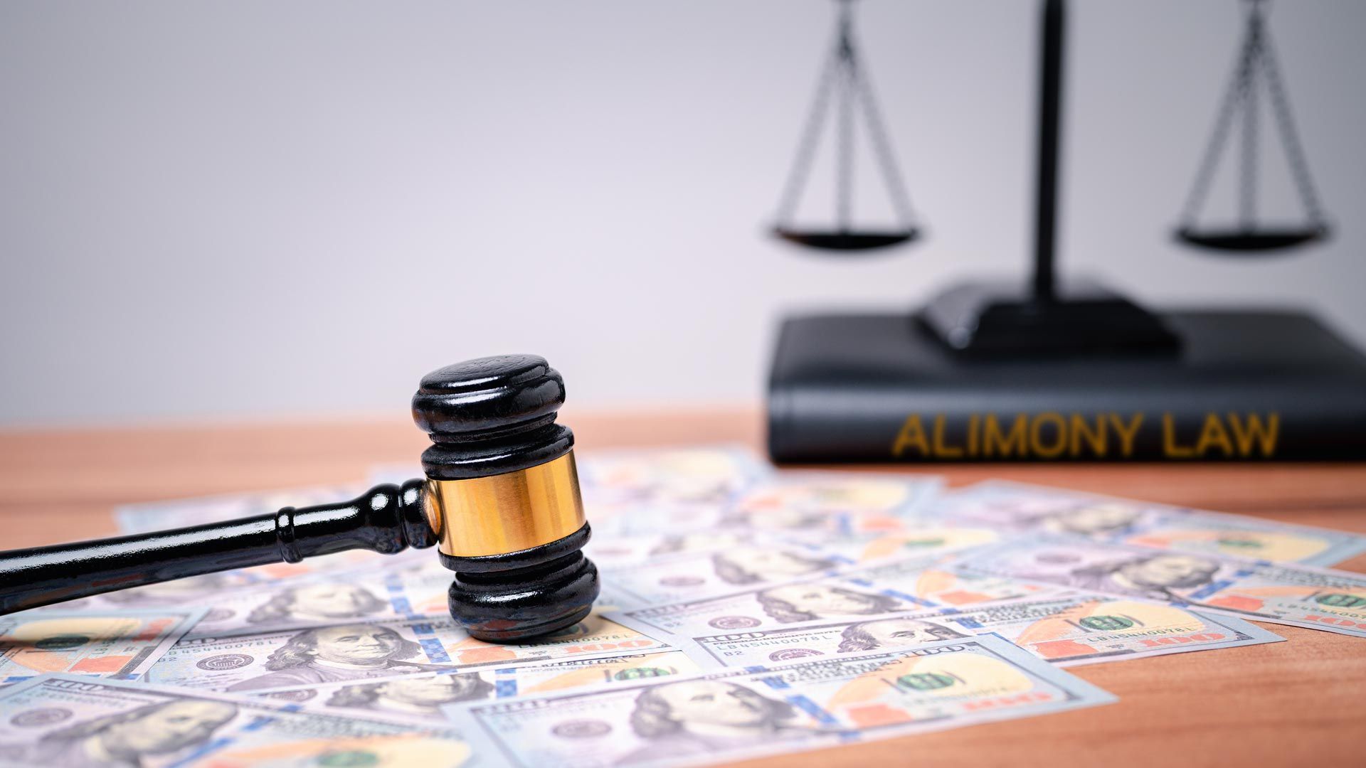 Gavel resting on hundred-dollar bills beside a scale of justice and an alimony law book Gavel resting on hundred-dollar bills beside a scale of justice and an alimony law book