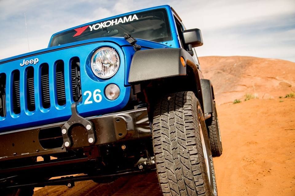 Blue Jeep off-roading on a sandy desert dune, front wheel angled toward the camera
