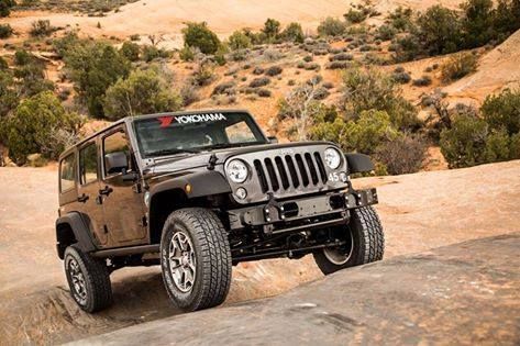 Black Jeep Wrangler driving over rocky desert terrain with a sandy hillside in the background