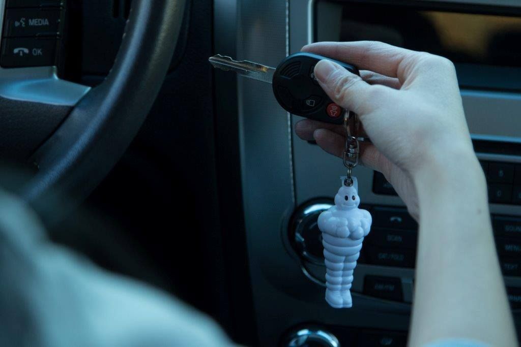 Hand holding car keys with a white rabbit keychain near the ignition in a car interior