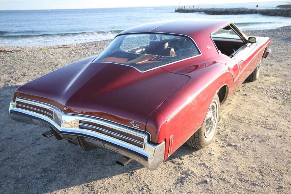 Red vintage car parked on a sandy beach by the ocean