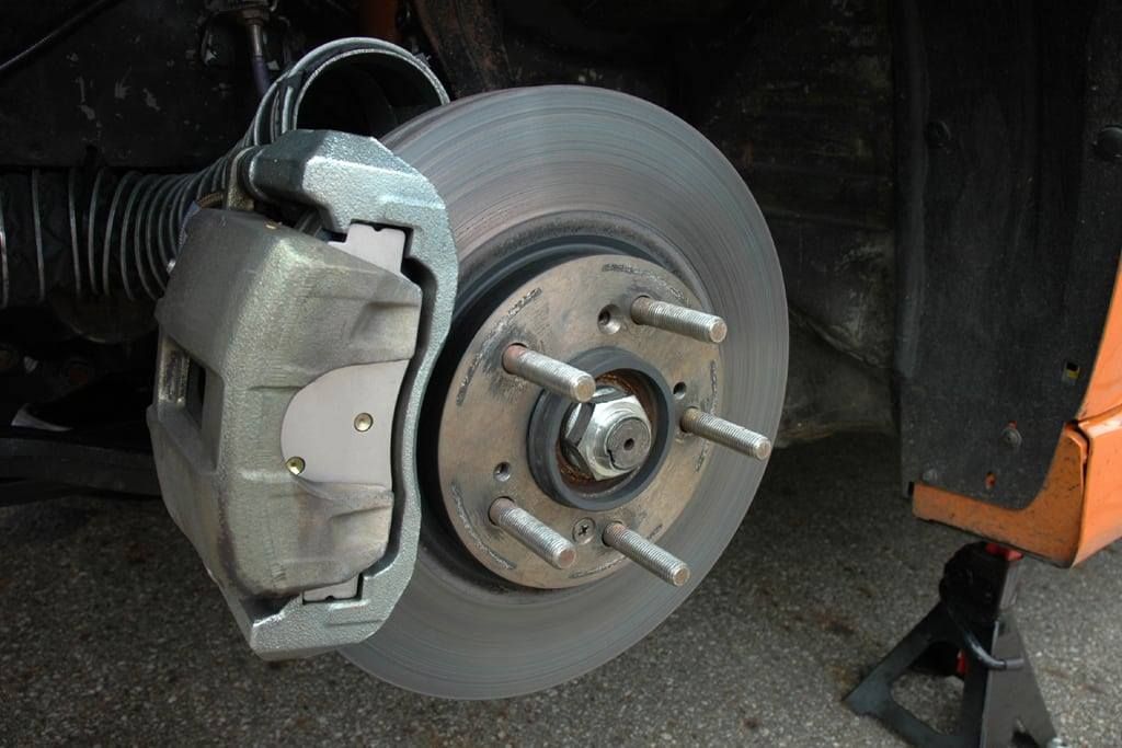 Car wheel with brake rotor, caliper, and lug studs visible on a vehicle lift