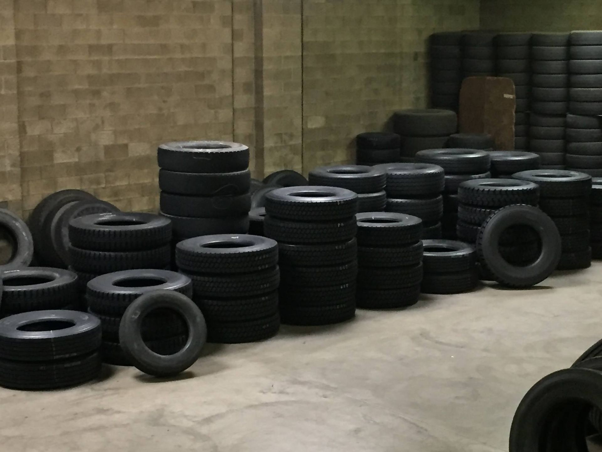 Stacks of black tires piled against a brick wall in a warehouse garage.