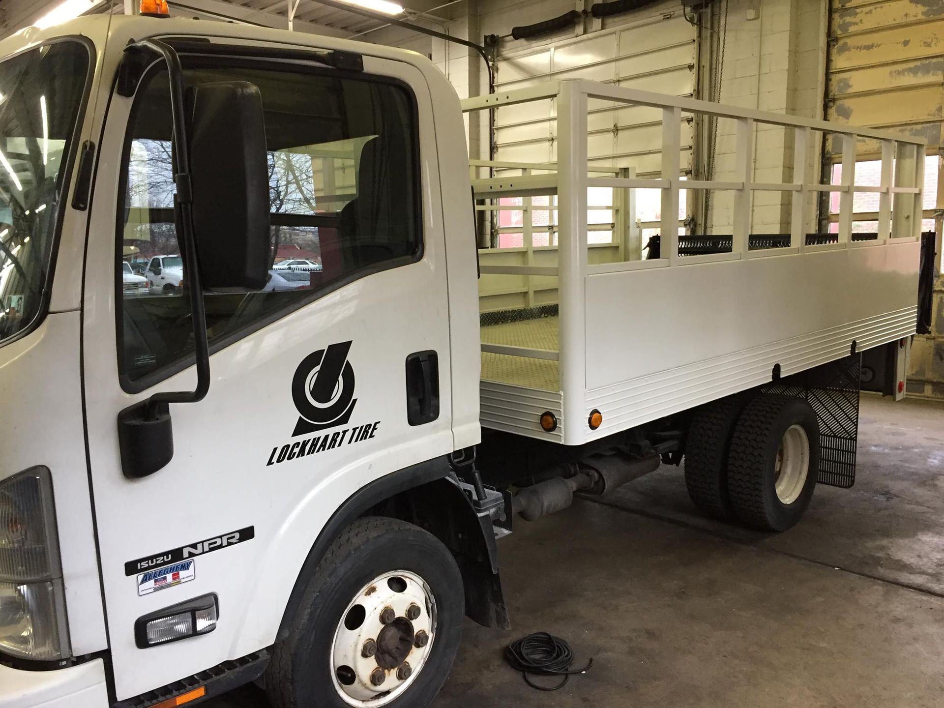 White flatbed truck parked indoors in a warehouse, side view of the cab and cargo bed.