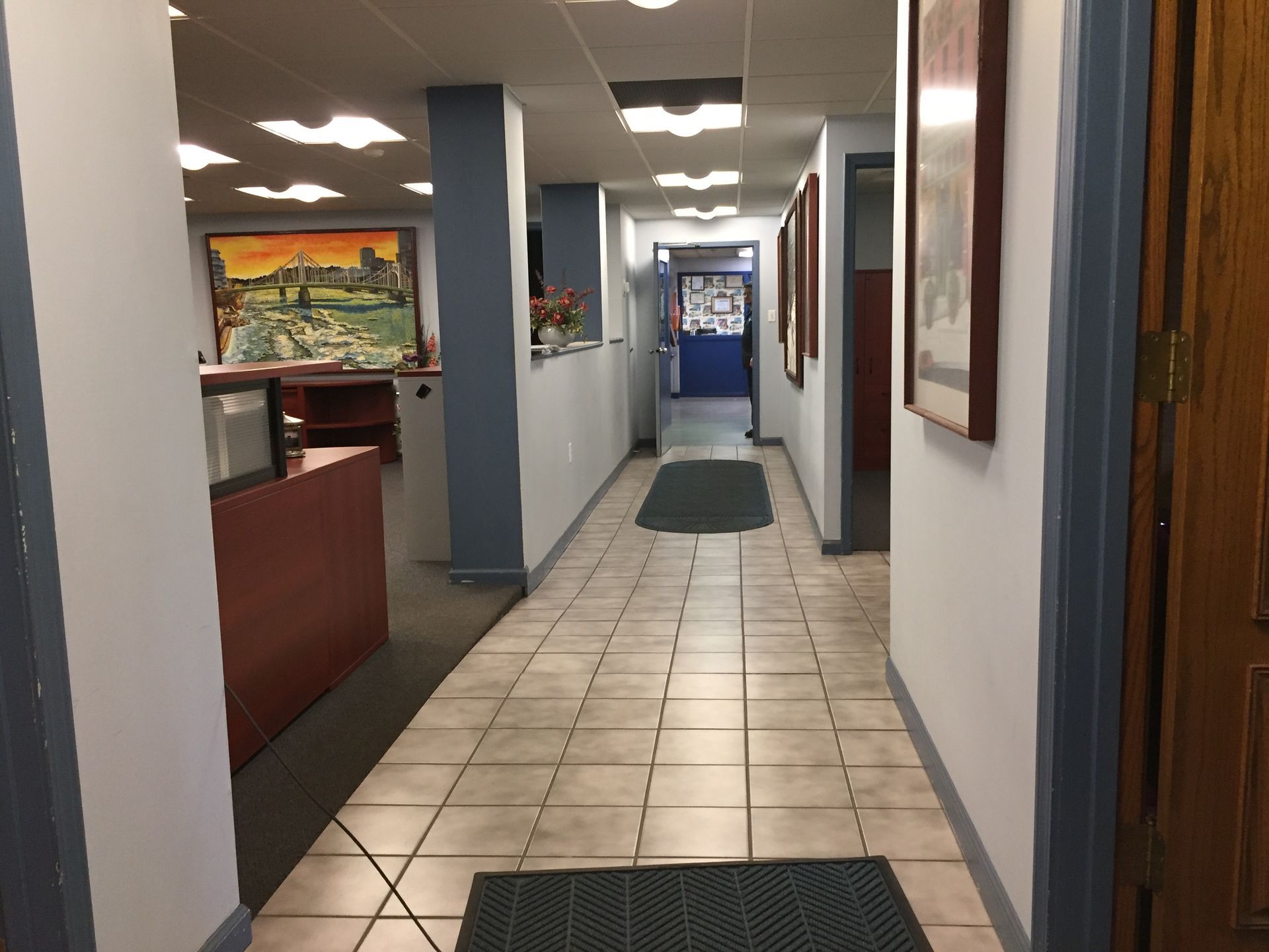 Office hallway with tiled floor, white walls, blue columns, and red reception desk
