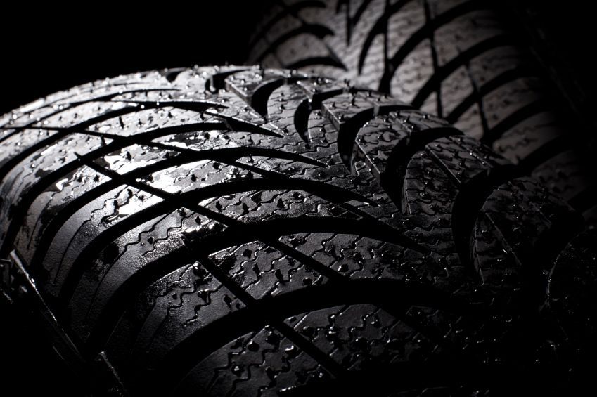 Close-up of a black tire tread with raindrops, lit by dramatic side light