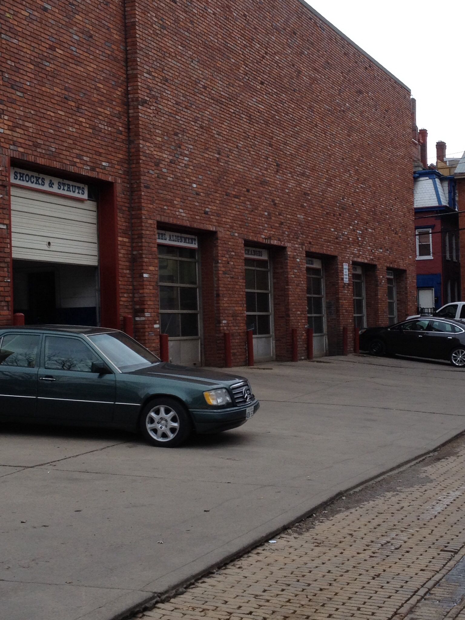 Brick industrial building with parked cars along a paved street on an overcast day