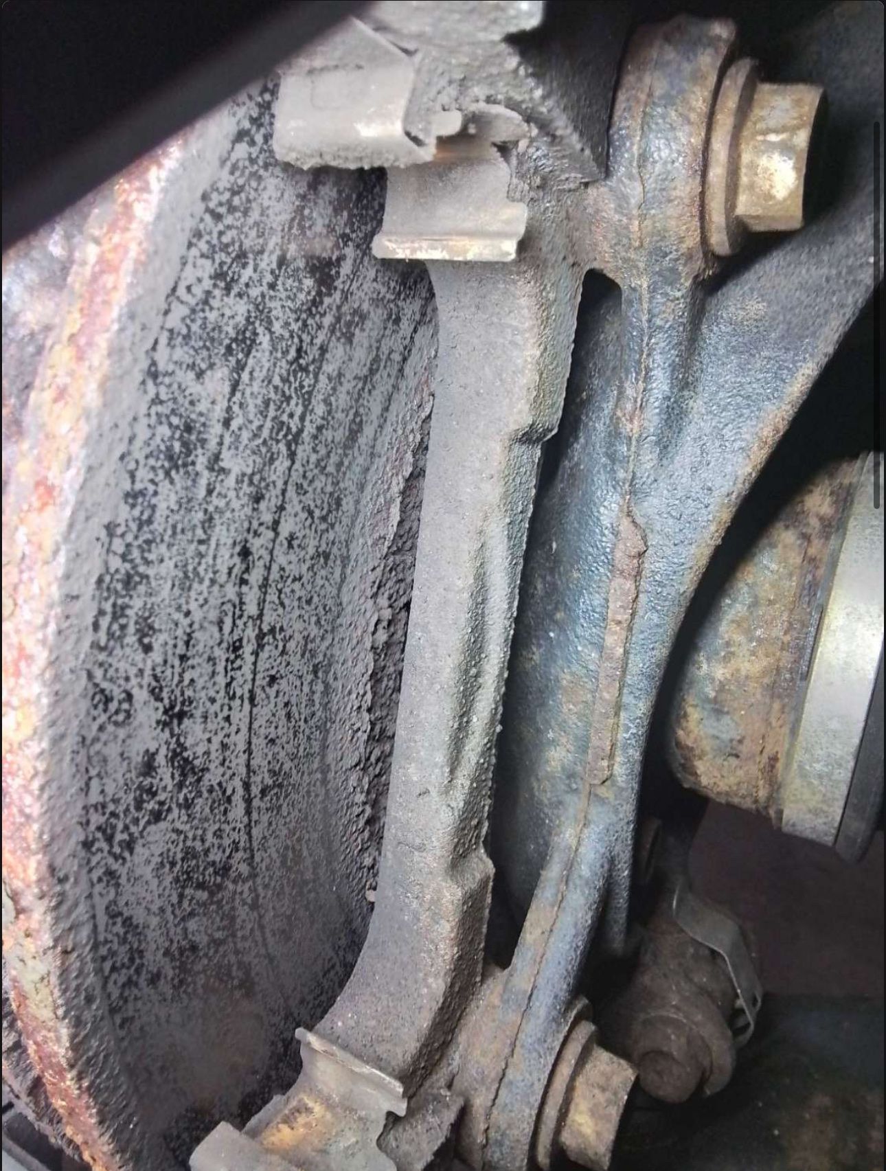 Close-up of a worn brake rotor and caliper assembly with rust and dust buildup.