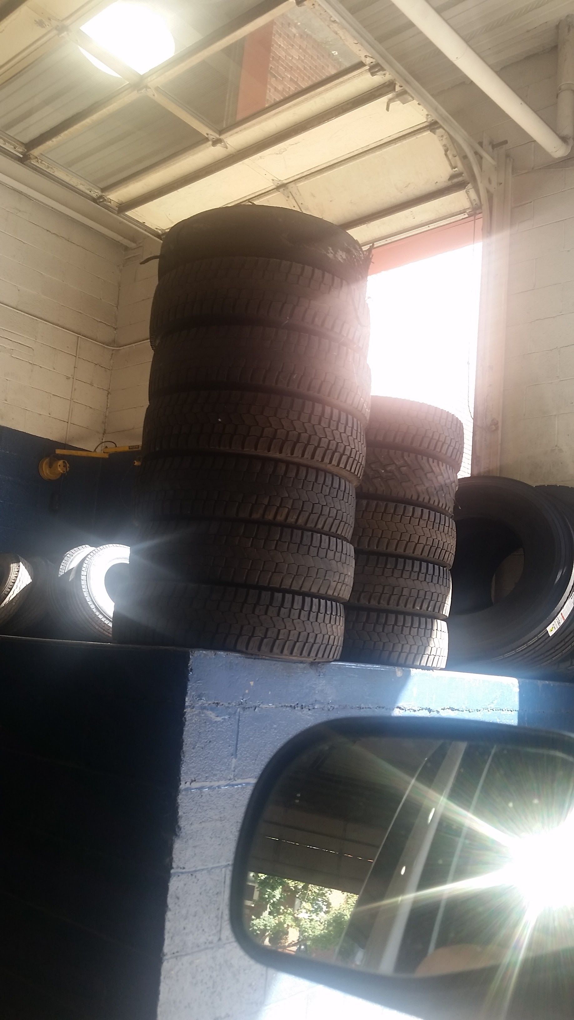 Stacks of dark tires in a vehicle cargo area under a metal roof with a side mirror visible