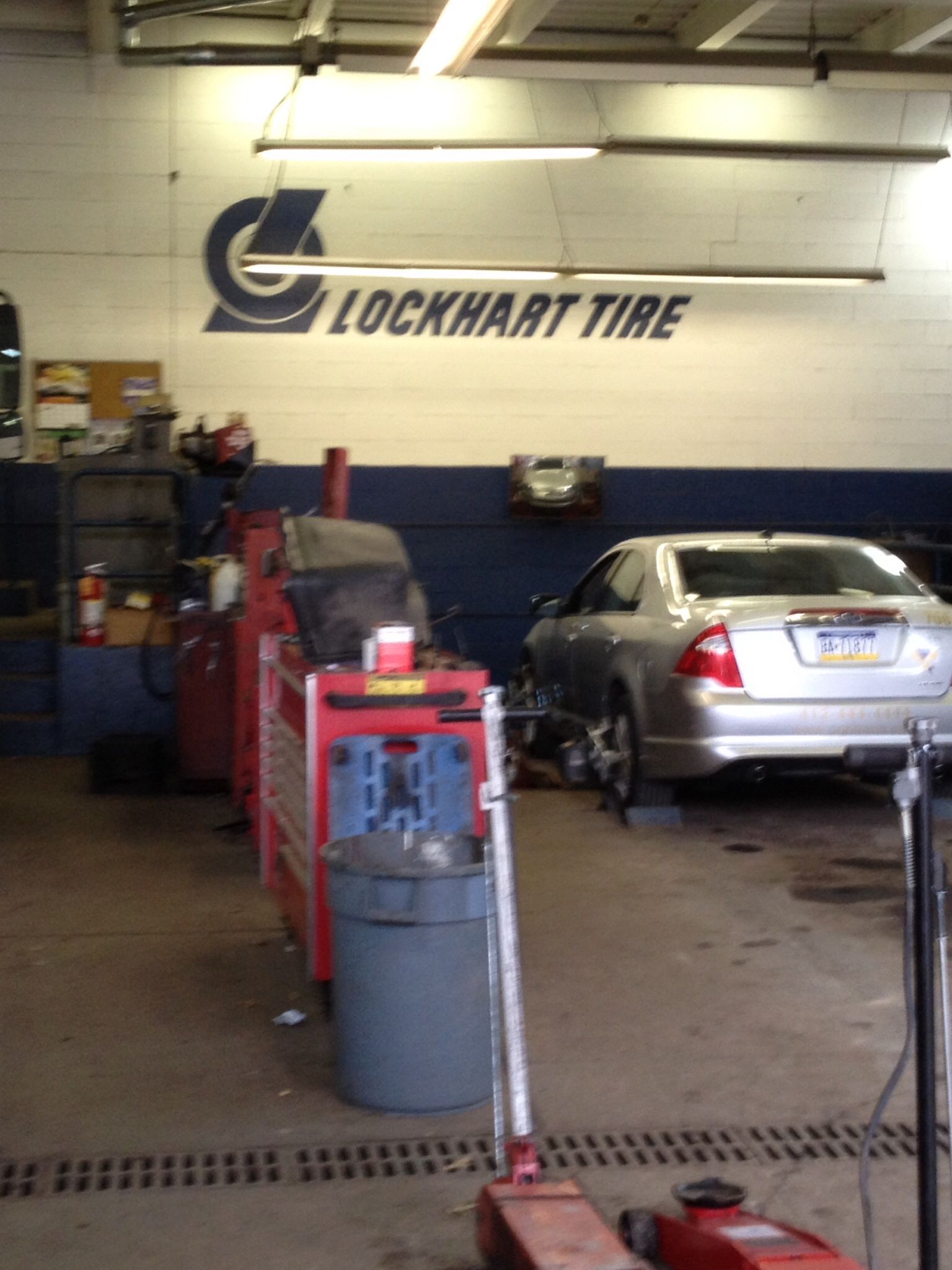 Auto repair shop interior with silver car on a lift and Lockhart Tire sign on the wall