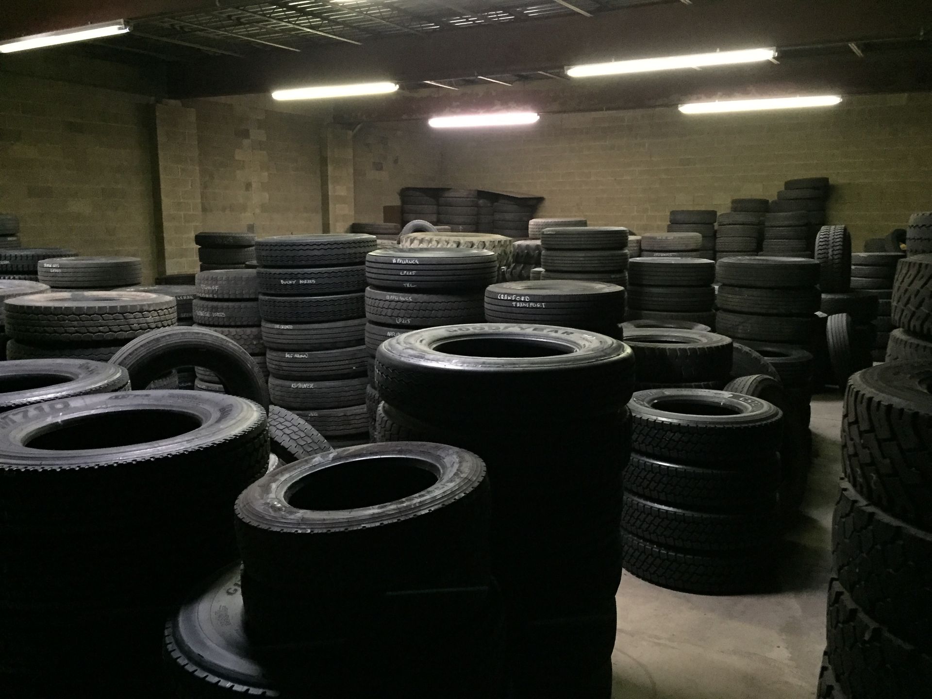 Rows of stacked black tires in a dim warehouse with concrete walls and overhead lights