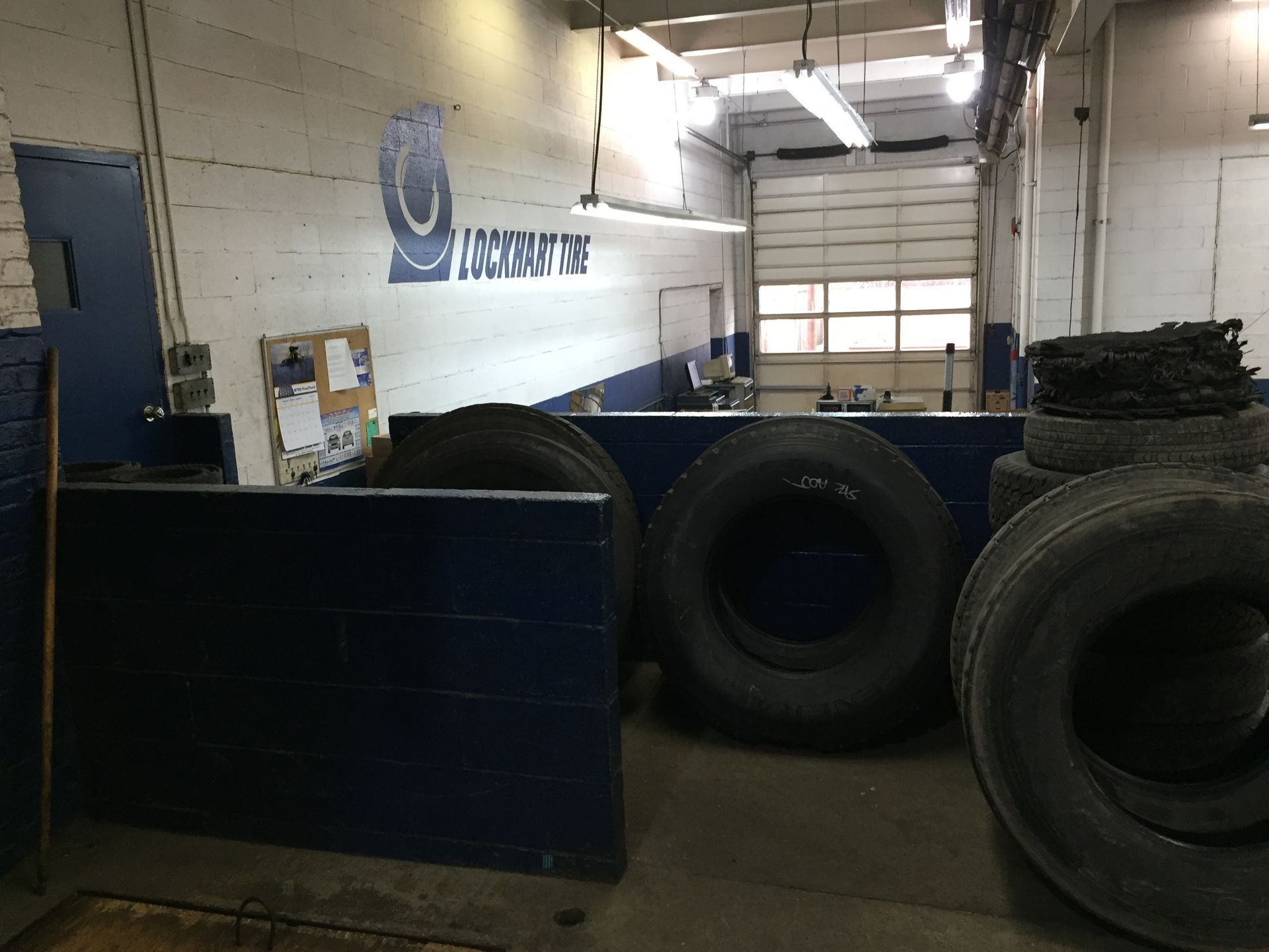 Warehouse with large tires stacked near a blue barrier and a garage door in the background
