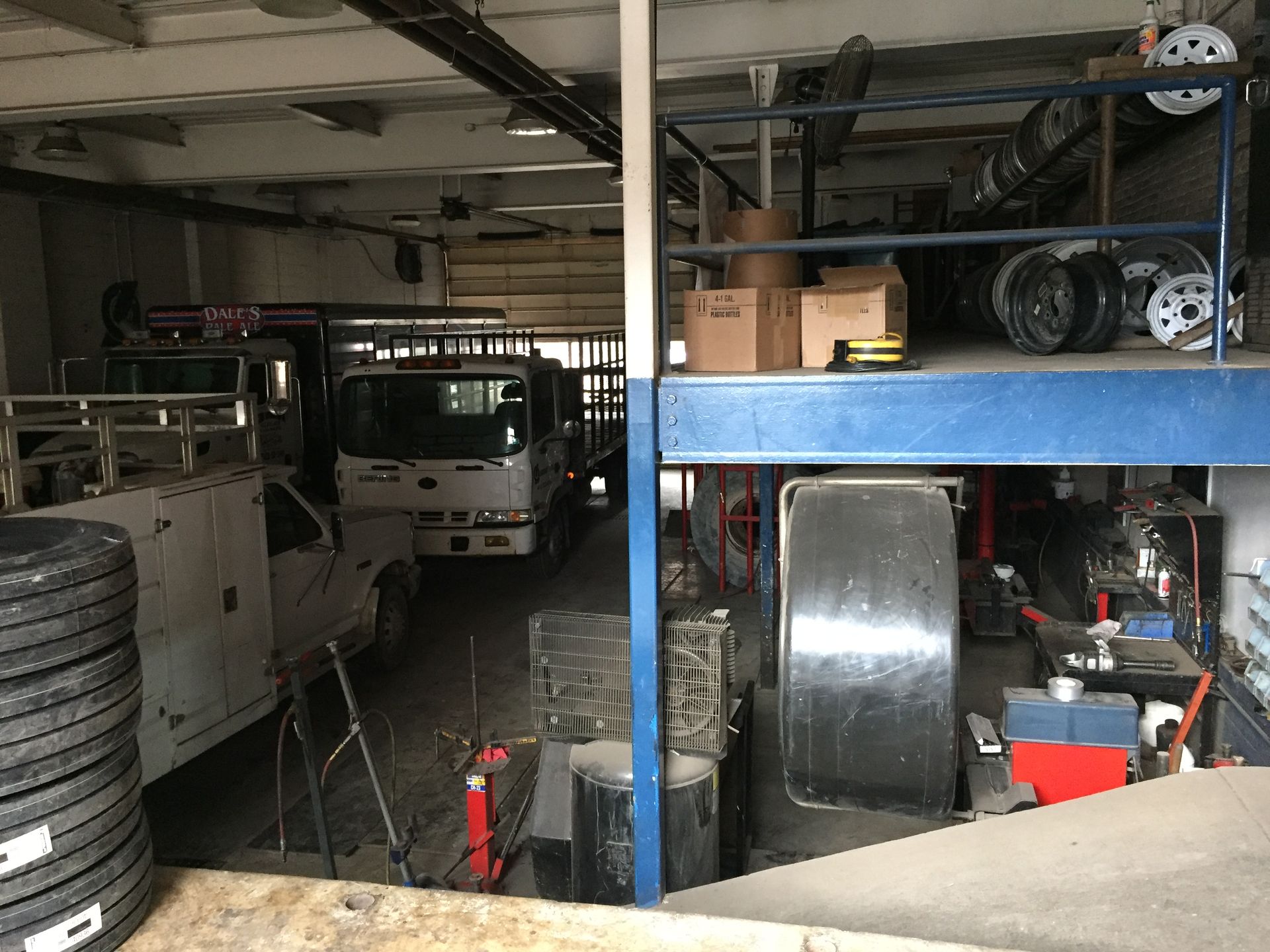Dim garage with parked white vehicles, stacked tires, and blue metal shelving packed with auto parts.