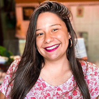 Uma mulher de cabelos longos está sorrindo e vestindo uma camisa rosa.