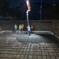 Construction crew pouring concrete at night, with a crane hose over a rebar foundation slab.