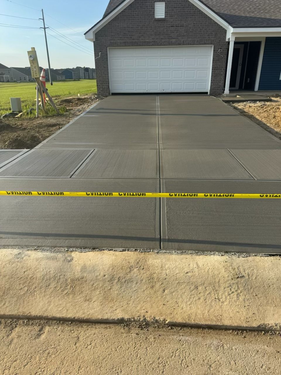 Freshly poured concrete driveway in front of a white garage with yellow caution tape across it