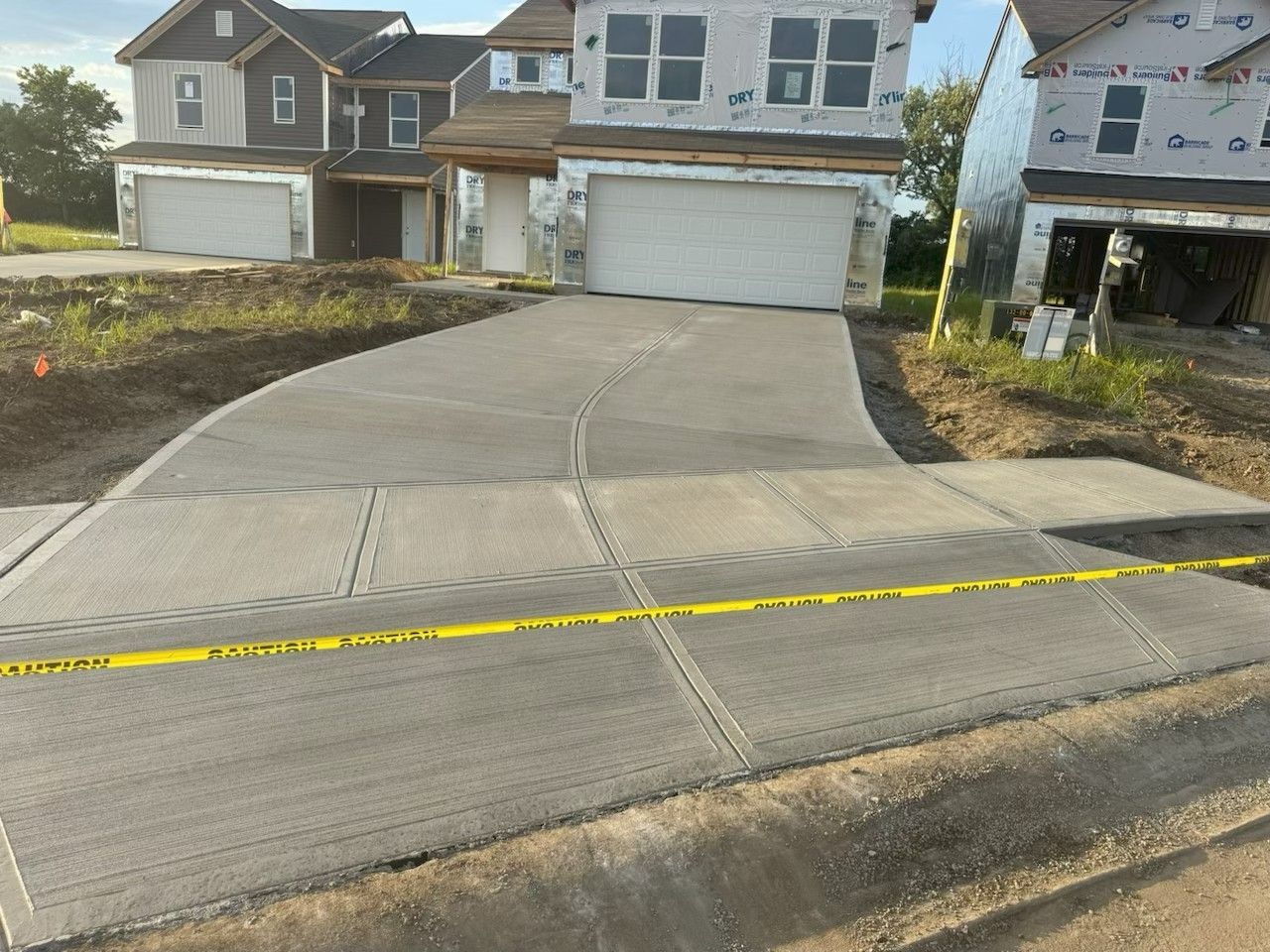 Suburban townhouse driveway under construction with yellow caution tape across the front entrance.