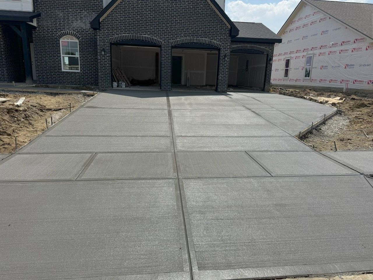 New concrete driveway leading to a brick house under construction