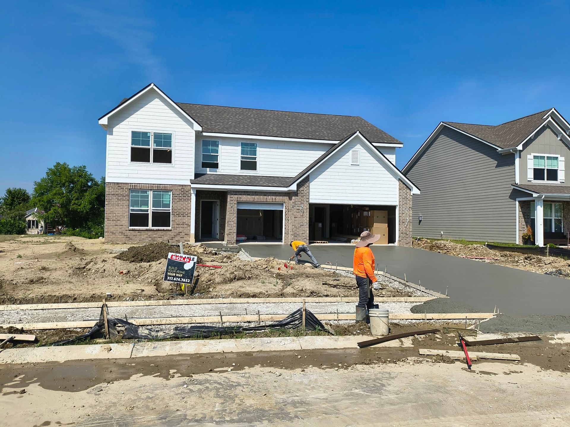 New house under construction with workers and a paved driveway in front