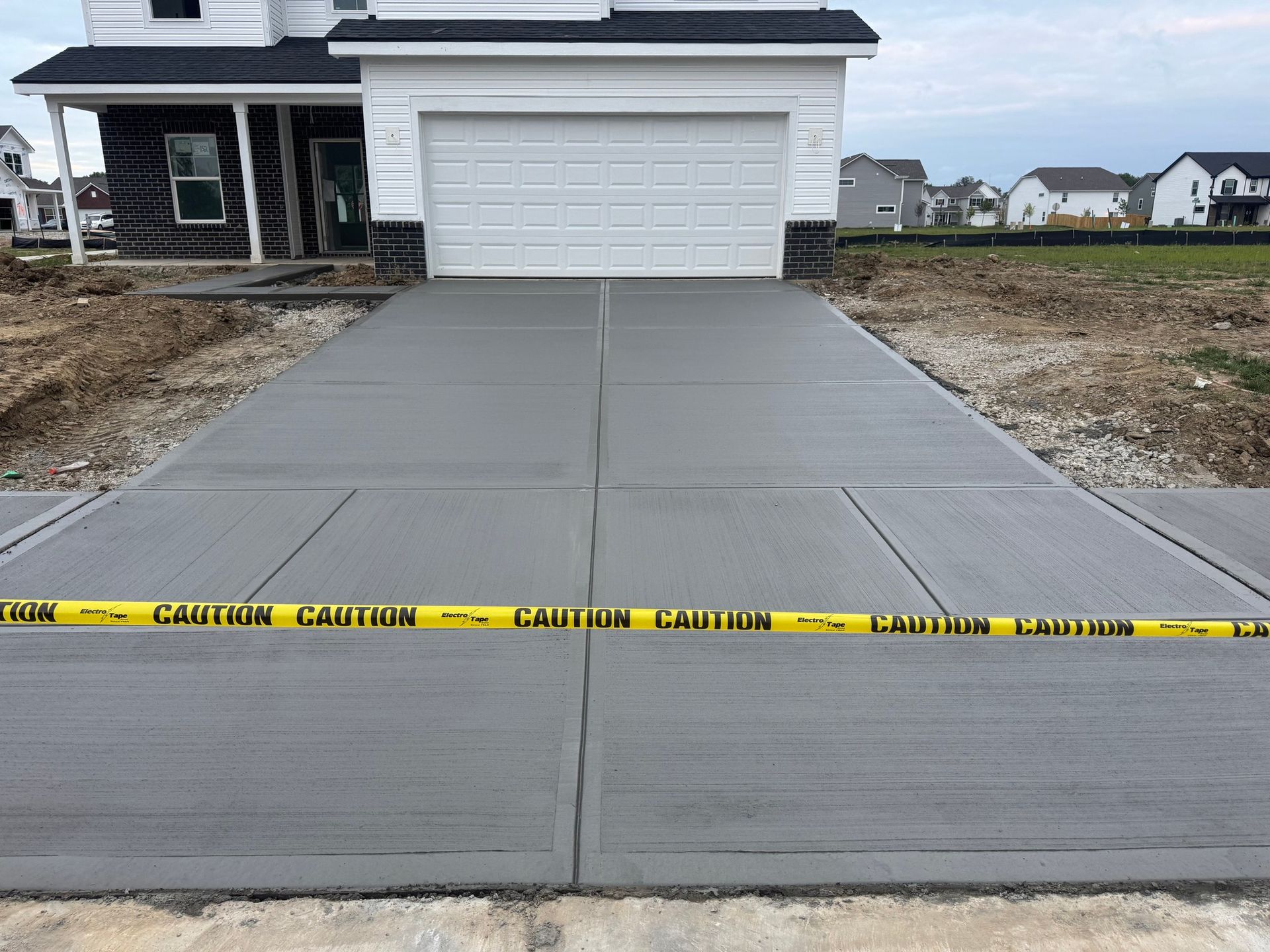 Fresh concrete driveway in front of a garage, bordered with caution tape at a new house.