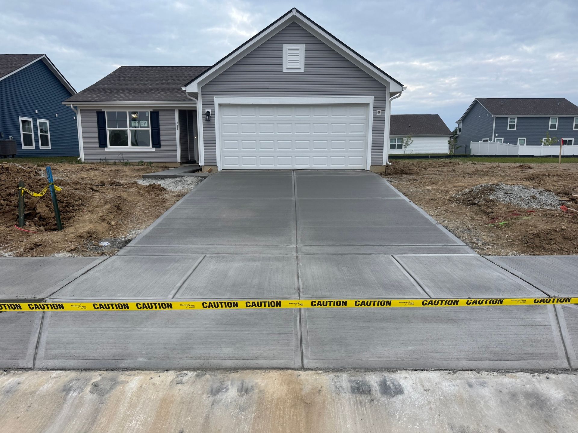 New concrete driveway leading to a gray garage with caution tape across the front