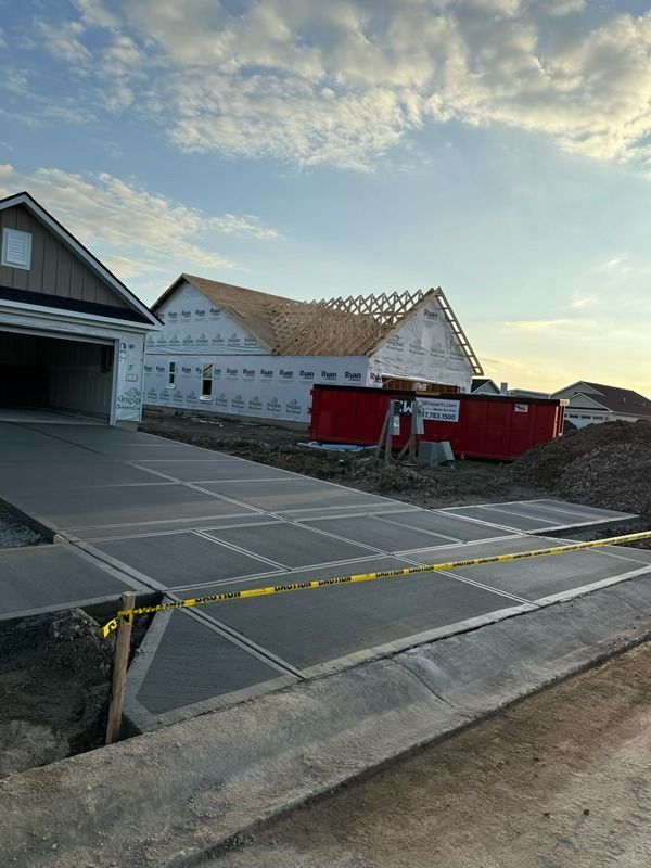 Residential construction site with framed house, red dumpster, and driveway taped off under a partly cloudy sky