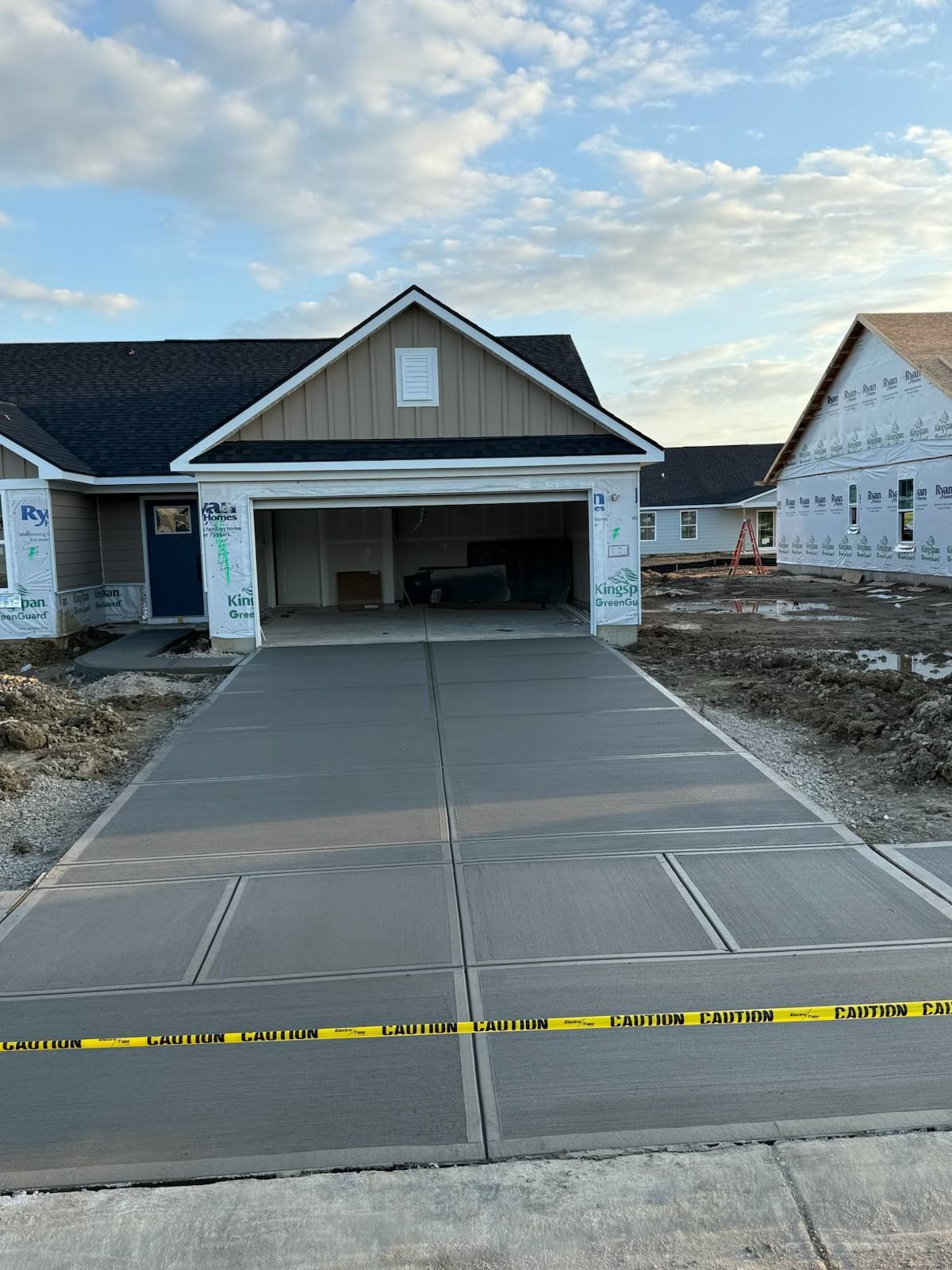 New concrete driveway leading to a house under construction with open garage.