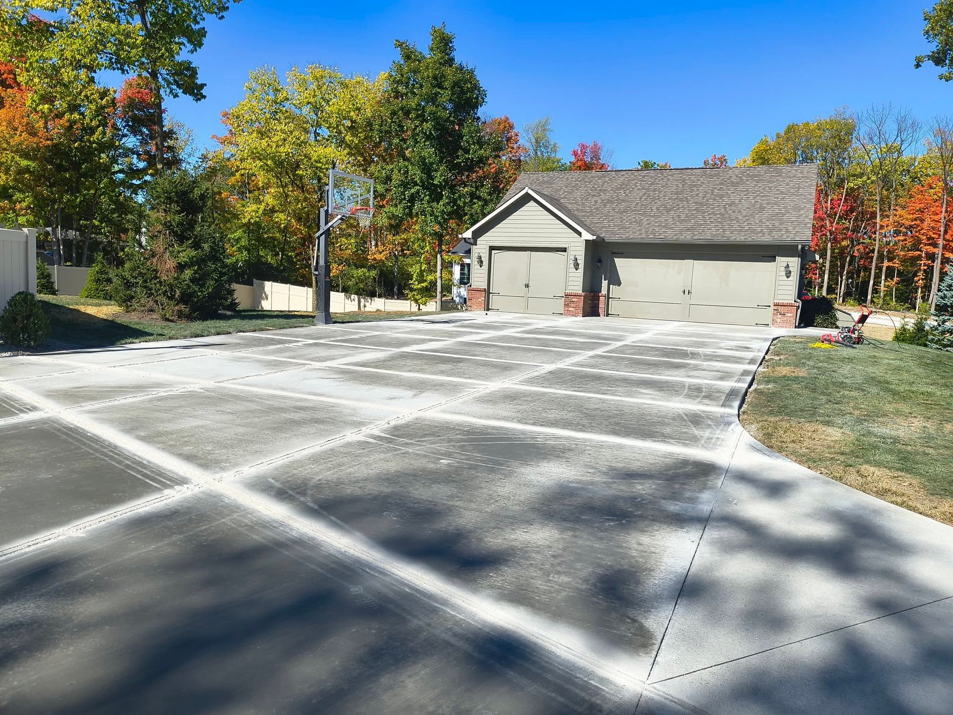 Suburban house with large concrete driveway, surrounded by autumn trees under a clear blue sky