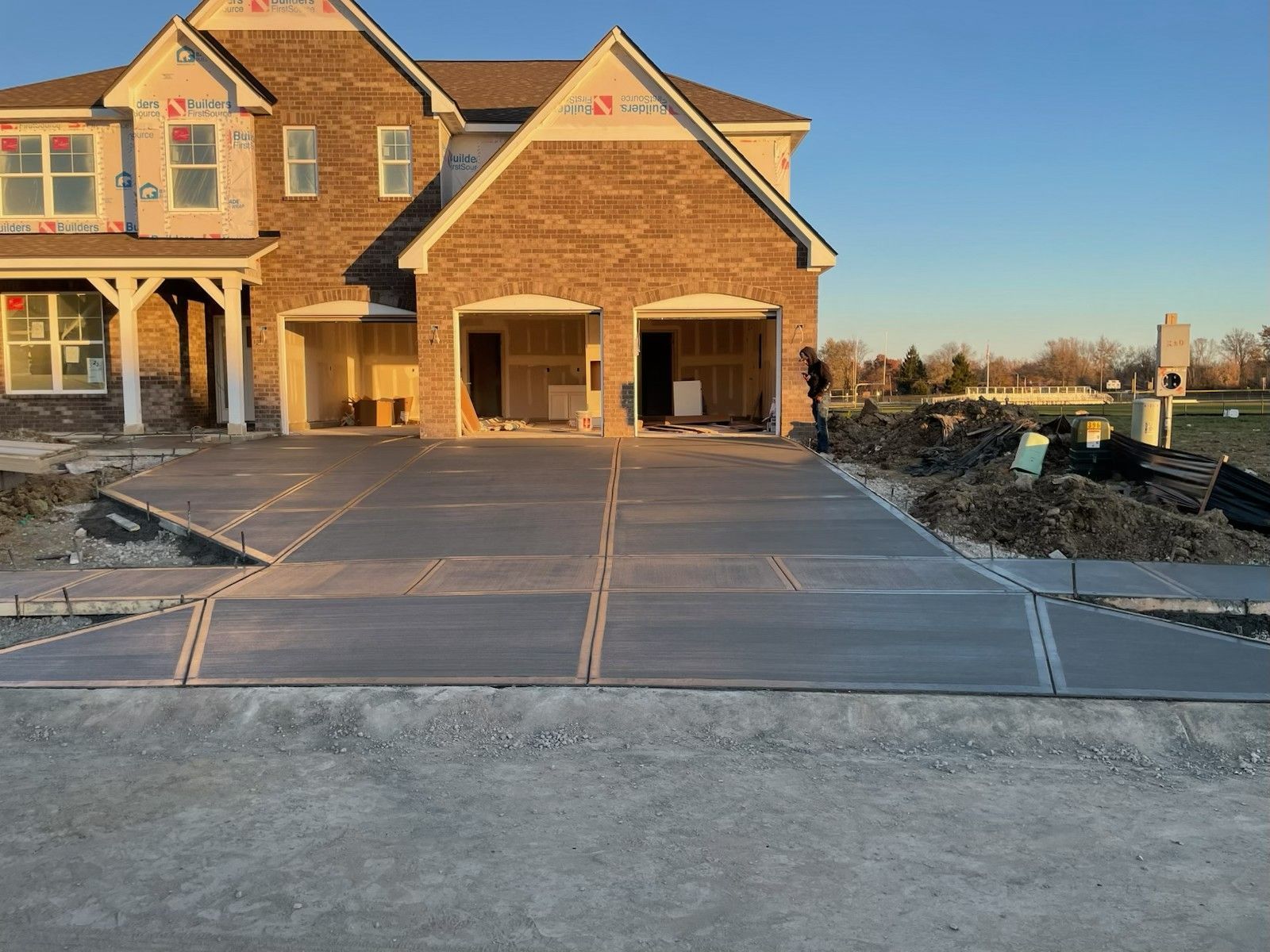 New suburban house with two-car garage and unfinished concrete driveway at sunset