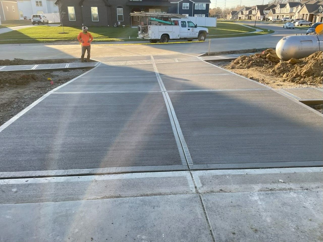New concrete sidewalk ramp leading to a neighborhood street, with a worker and houses in the background
