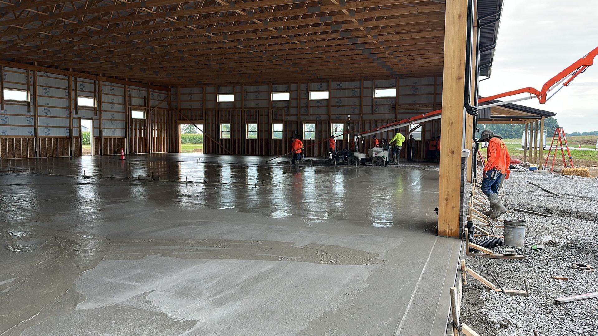 Large open construction site with a concrete floor, workers, and equipment inside a steel-framed building