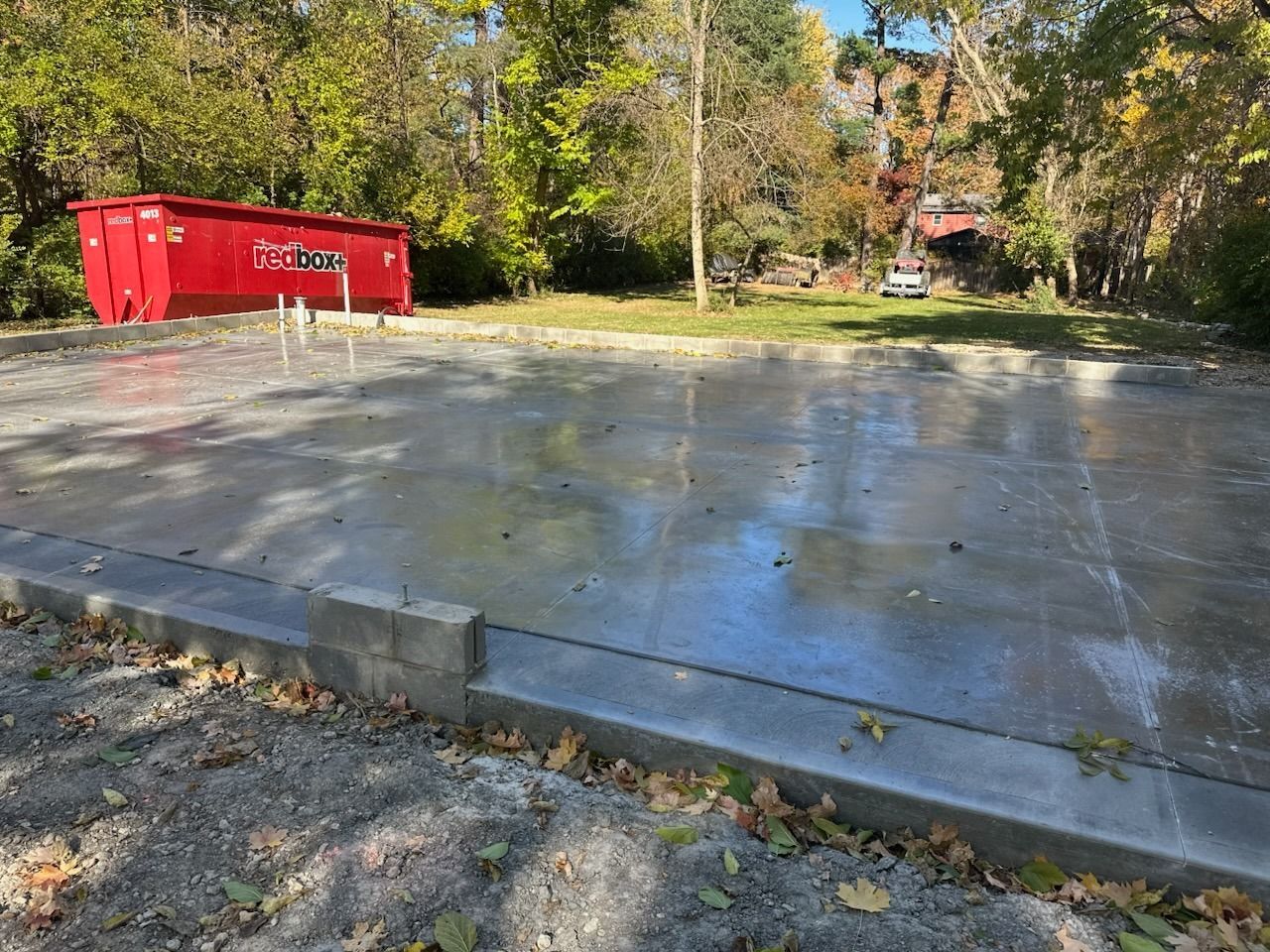 Concrete pad beside a red dumpster in a wooded outdoor lot