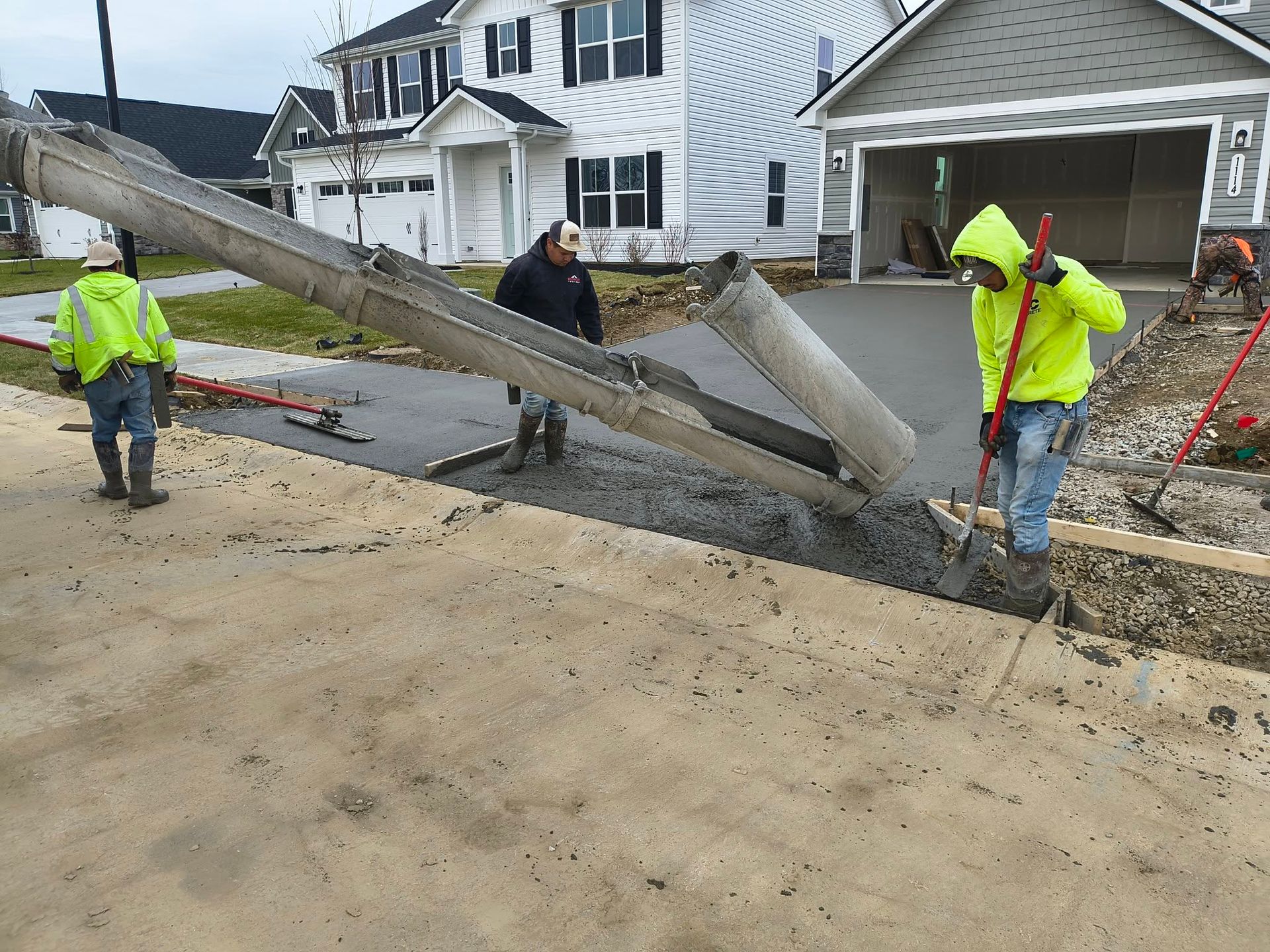 Utility workers repair a broken utility pole on a residential street near houses and a garage.