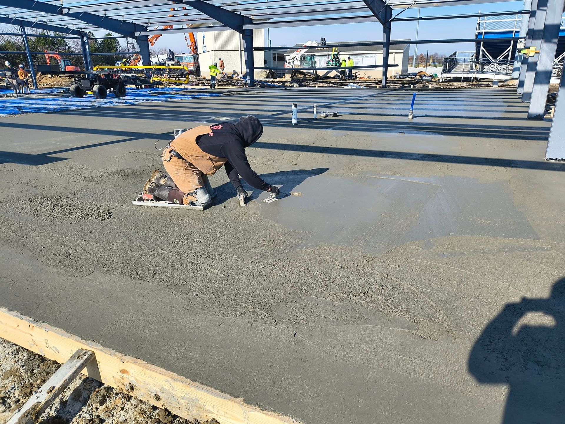 Worker smoothing wet concrete at a construction site with steel beams overhead