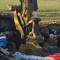 Excavator bucket digging beside a large pipe at a muddy construction site in a field