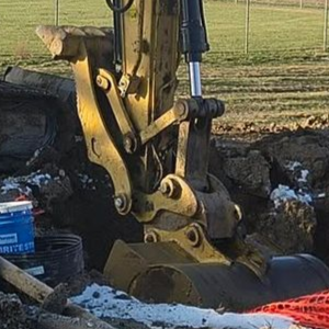 Excavator bucket digging beside a large pipe at a muddy construction site in a field