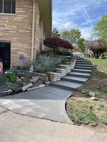 Curved concrete walkway leading to stone steps and a landscaped house entrance with shrubs and trees