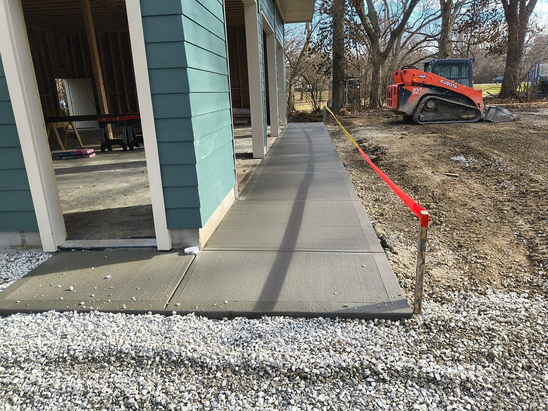 Covered walkway beside a house with a ramp, gravel path, and an orange utility vehicle in the yard.