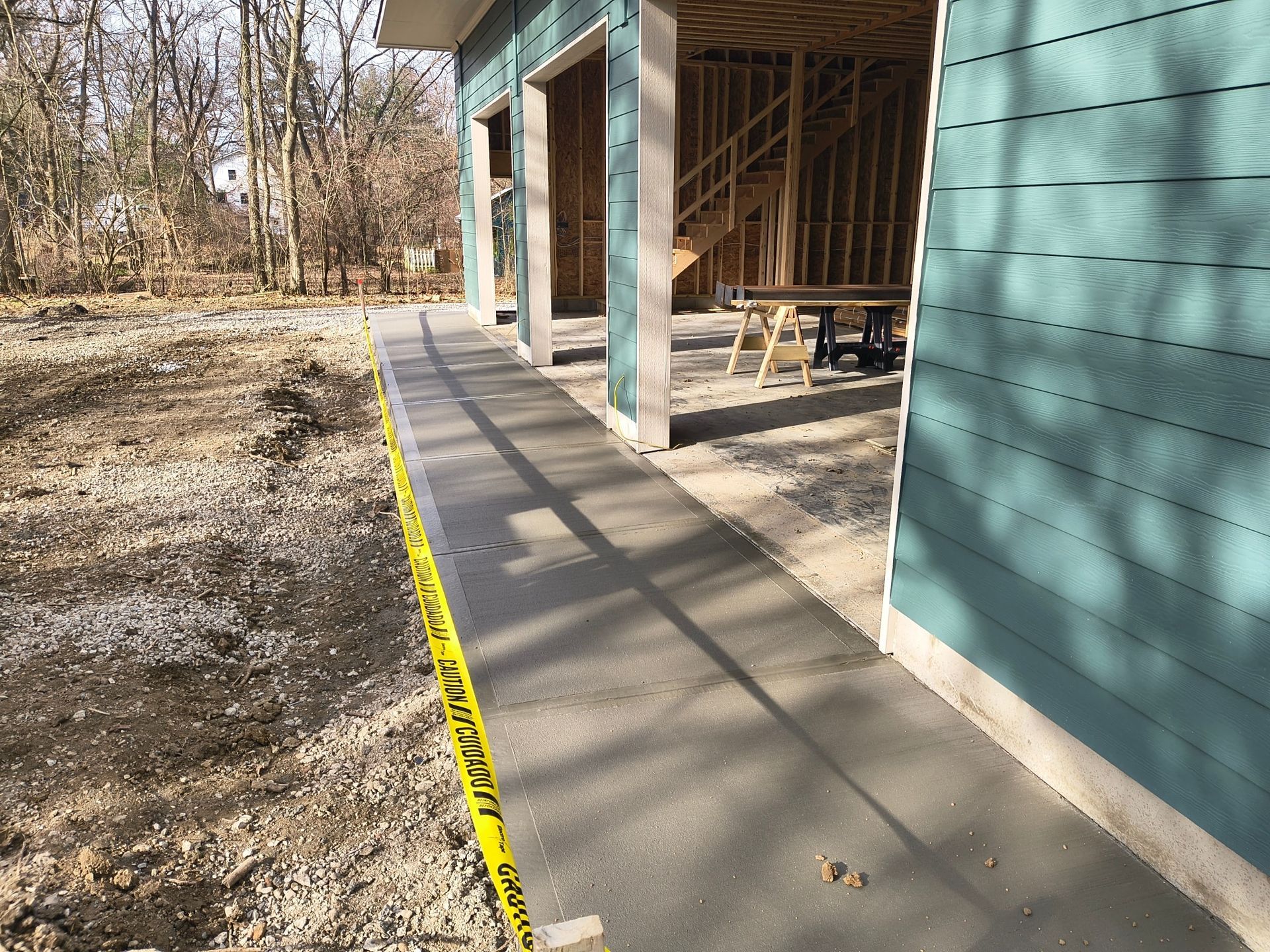 Concrete walkway beside a teal building under construction, with yellow caution tape along the edge.