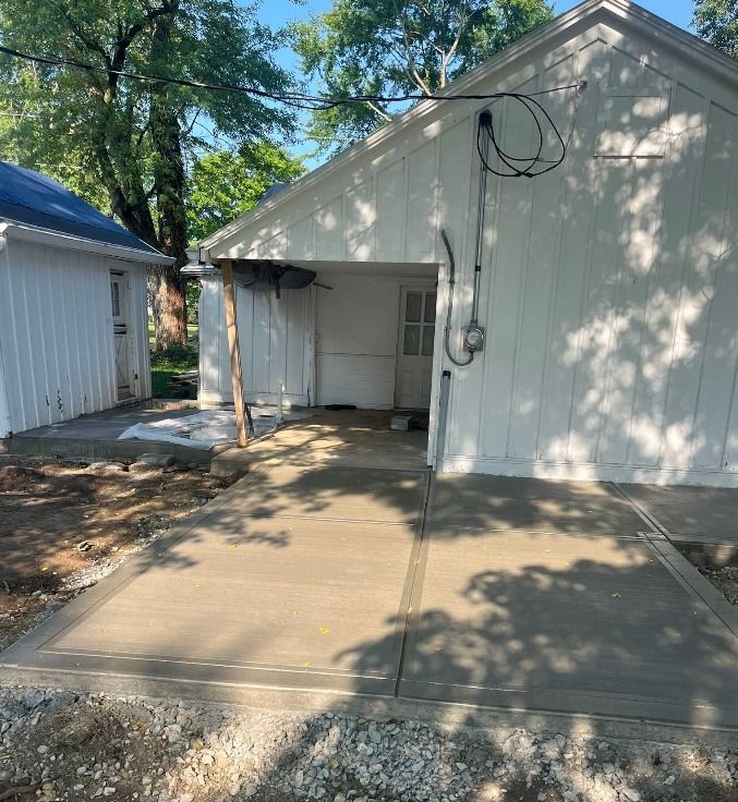 White garage with open bay and concrete driveway in a backyard, with coiled cables near the roof.