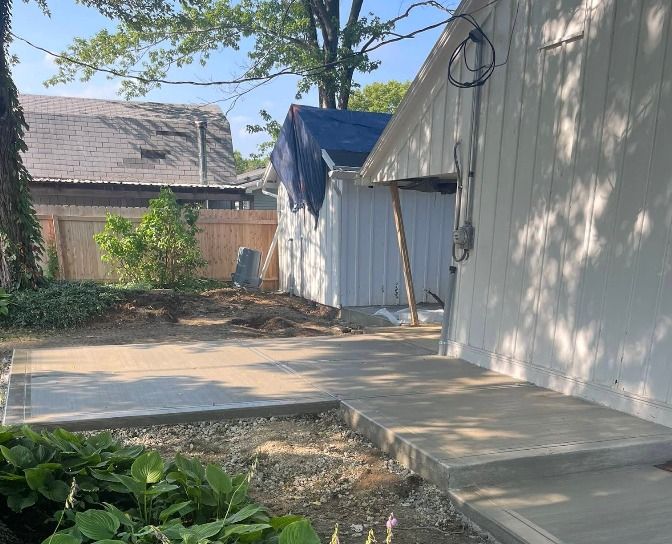 Backyard walkway beside a white house, with a blue tarp over a small structure and a shaded patio area
